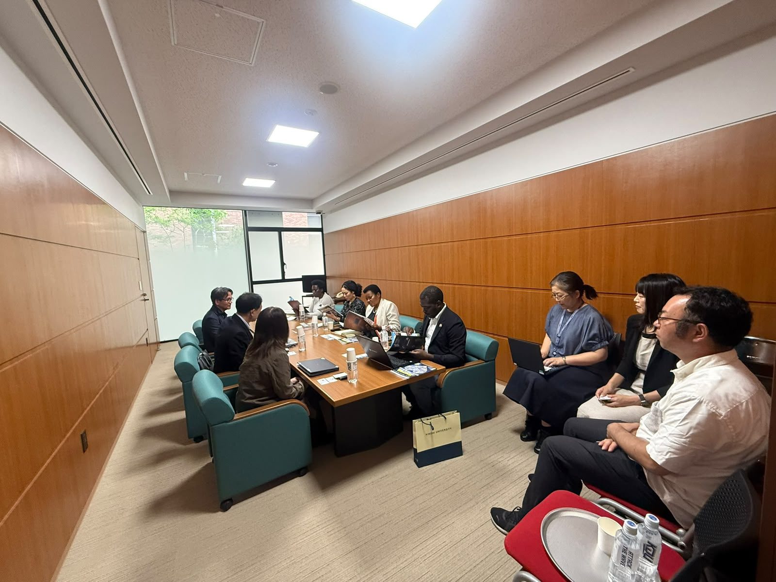 A group in a meeting room, with a Kindai University gift bag visible on the floor