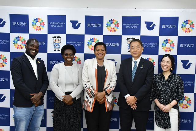 A group posing with the Mayor of Higashiosaka City in front of a Higashiosaka SDGs backdrop