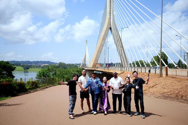A mixed Ugandan and Japanese group posing in front of a cable-stayed bridge in Jinja, Uganda