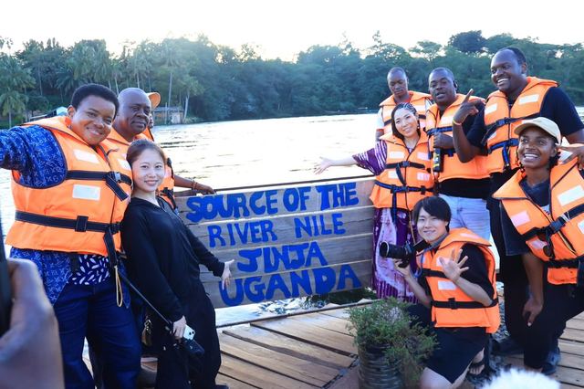 A mixed Ugandan and Japanese group at the "Source of the River Nile, Jinja Uganda" sign, wearing life vests